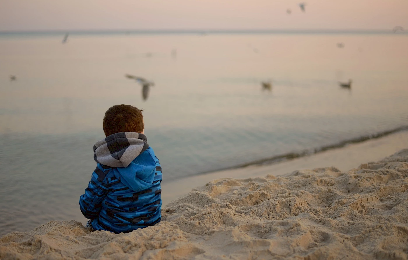 Hallin Löfgren Juristbyrå - En ung pojke sitter på stranden och tittar ut mot havet.